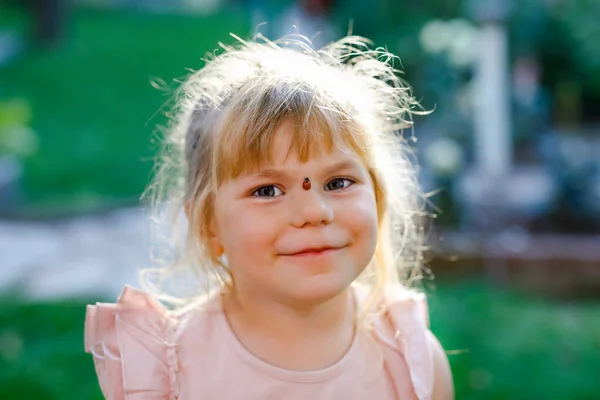 Porträt eines kleinen Mädchens mit Marienkäfer im Gesicht. Glücklich lächelndes aufgeregtes Kind an einem warmen, sonnigen Sommertag. — Stockfoto