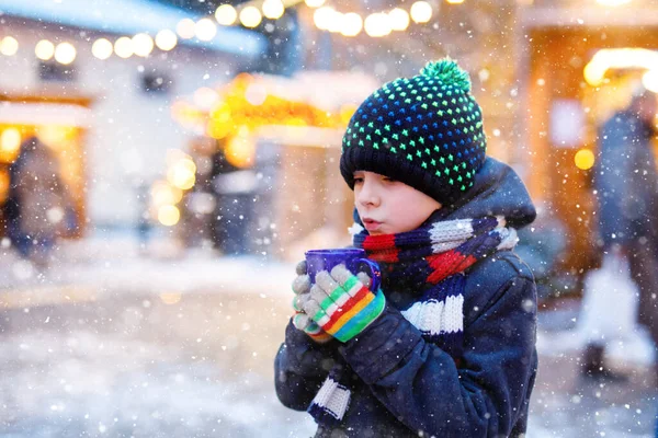 Little cute kid boy drinking hot children punch or chocolate on German Christmas market. Happy child on traditional family market in Germany, Laughing boy in colorful winter clothes — Stock Photo, Image