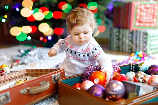 Adorable baby girl holding colorful lights garland in cute hands. Little child in festive clothes decorating Christmas tree with family. First celebration of traditional holiday called Weihnachten — Stock Photo, Image