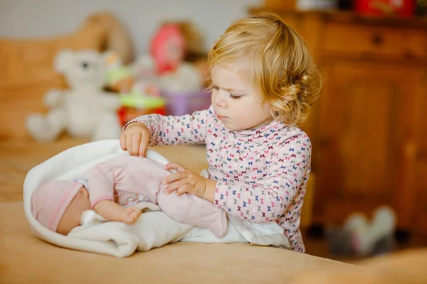 Schattig schattig klein peutermeisje dat met een pop speelt. Gelukkig gezond baby kind hebben plezier met rollenspel, spelen moeder thuis of kinderkamer. Actieve dochter met speelgoed. — Stockfoto