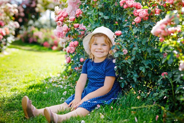 開花中の小さな幼児の少女の肖像画は庭をバラした。夏の晴れた日に公園でバラや花を楽しんでいるかわいい美しい子供。幸せな笑顔の赤ちゃん. — ストック写真