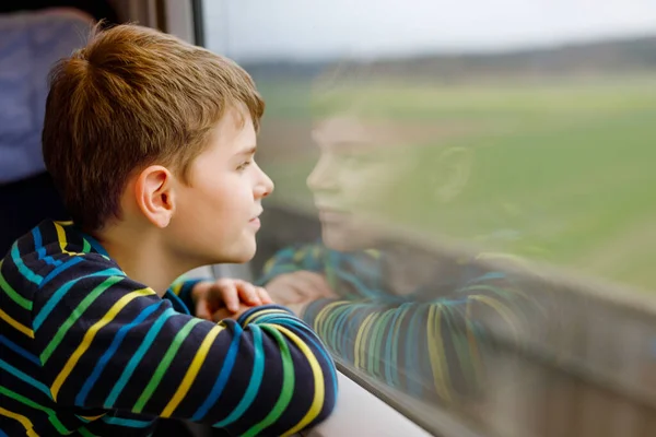 Menino adorável viajando de trem. Criança sorridente feliz olhando pela janela durante o movimento do trem. Miúdo a sonhar e a pensar. Férias em família e viagem . — Fotografia de Stock