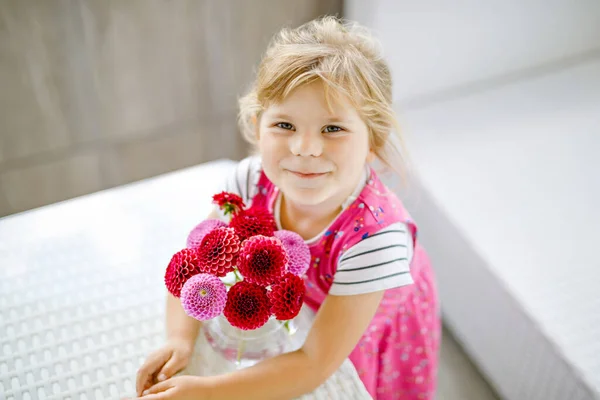 Portrait de petite fille en bas âge admirant le bouquet de fleurs dahlia rouges et roses en fleurs. Mignon enfant heureux sentant et comptant fleur le jour ensoleillé d'été. — Photo