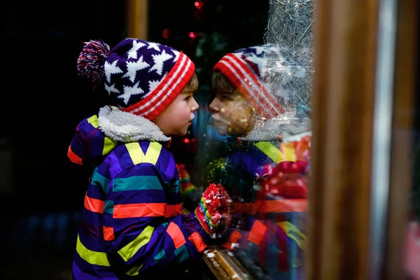 Roztomilý malý, zdravý školák na vánočním trhu. Vtipné šťastné dítě v módě zimní oblečení, aby okno nakupování zdobené dárky, vánoční strom. Padá sníh, padá sníh — Stock fotografie