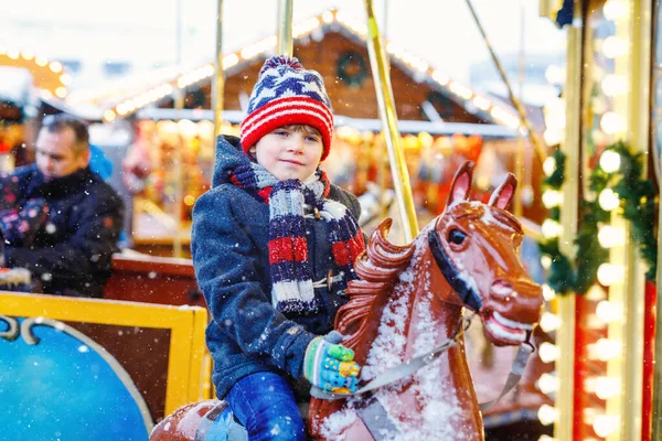 Adorabile ragazzino che cavalca su un allegro cavallino giostra al luna park o al mercatino di Natale, all'aperto. Bambino felice divertirsi sul tradizionale mercato di Natale in famiglia in Germania — Foto Stock