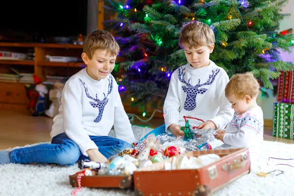 Δύο μικρά αγοράκια και ένα αξιολάτρευτο κοριτσάκι που διακοσμούν το χριστουγεννιάτικο δέντρο με παλιά vintage παιχνίδια και μπάλες. Οικογενειακή γιορτή των οικογενειακών διακοπών. Τρία παιδιά, αδέρφια και αδερφές στο σπίτι.. — Φωτογραφία Αρχείου