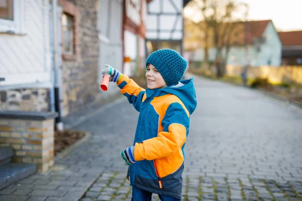 Little school kid boy of elementary class walking to school on cold winter day. Happy child having fun on a city street. Student with backpack in colorful winter clothes holding things for project — Stock Photo, Image