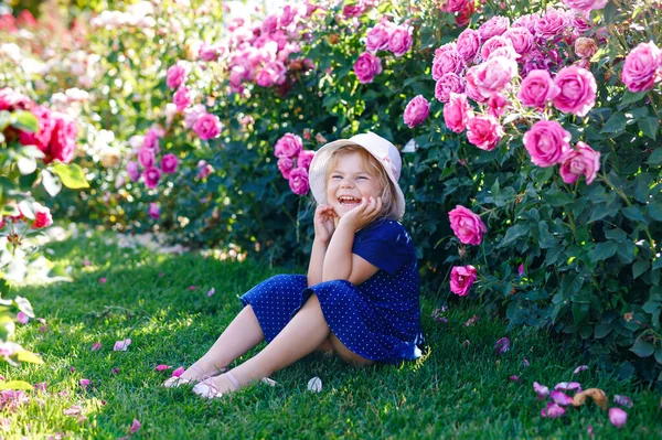 Portret van een kleuter in een bloeiende rozentuin. Schattig mooi mooi kind dat plezier heeft met rozen en bloemen in een park op zomerse zonnige dag. Gelukkig lachende baby. — Stockfoto