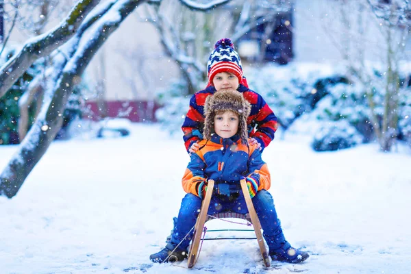 Two kid boys having fun sleigh ride during snowfall. Children sledding on snow. siblings riding a sledge. Twins play outdoors. Friends sled in snowy winter park. Active fun for family vacation — Stock Photo, Image