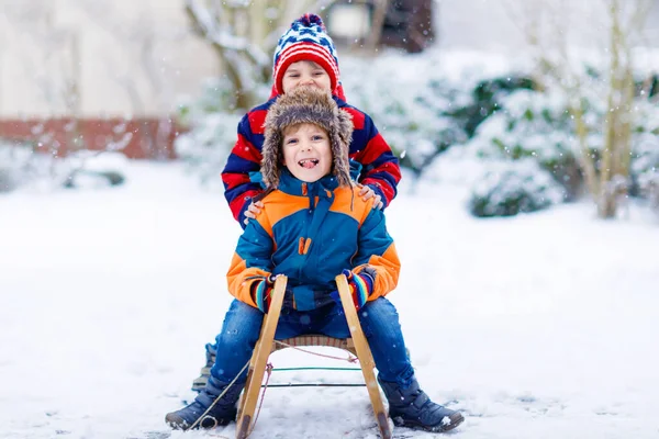 Two kid boys having fun sleigh ride during snowfall. Children sledding on snow. siblings riding a sledge. Twins play outdoors. Friends sled in snowy winter park. Active fun for family vacation — Stock Photo, Image