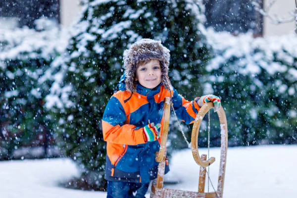 Little school boy having fun with sleigh ride during snowfall. Hapy child sledding on snow. Preschool kid riding a sledge. Child playing outdoors in snowy winter park catching snowflake. — Stock Photo, Image
