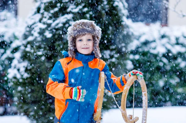 Niño de la escuela divirtiéndose con paseo en trineo durante las nevadas. Niño feliz en trineo en la nieve. Niño en edad preescolar montando un trineo. Niño jugando al aire libre en el parque de invierno nevado la captura de copo de nieve. —  Fotos de Stock