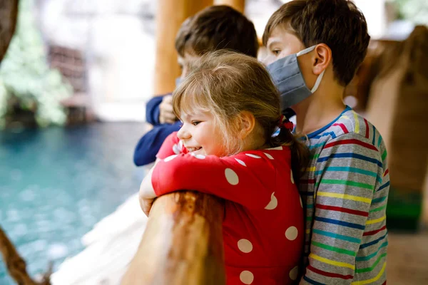 Zwei Jungen und ein Mädchen besuchen gemeinsam den Zoo. Drei Kinder beobachten Tiere und Insekten. Schüler tragen wegen der Coronavirus-Pandemie immer wieder Masken mit Medikamenten. Familie im Urlaub — Stockfoto