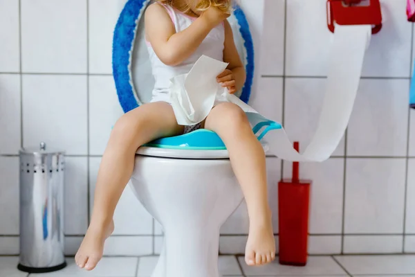 Closeup of cute little toddler baby girl child sitting on toilet wc seat. Potty training for small children. Unrecognizable face of child