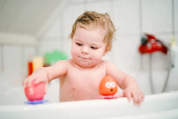 Schattig schattig baby meisje neemt schuimig bad in bad. Peuter spelen met bad rubber speelgoed. Mooi kind hebben plezier met kleurrijke kauwgom speelgoed en schuim bellen — Stockfoto