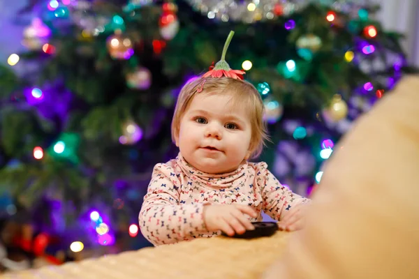 Portret małej uroczej dziewczynki uczącej się chodzić i stać. z choinką i światełkami na tle. Urocza córeczka w domu. Piękne dziecko w ubraniu casual — Zdjęcie stockowe