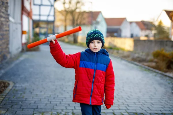寒い冬の日に小学校の子供の男の子が学校に歩いています。幸せな子供は街の通りで楽しんでいます。プロジェクトのためのものを保持するカラフルな冬服のバックパックを持つ学生 — ストック写真