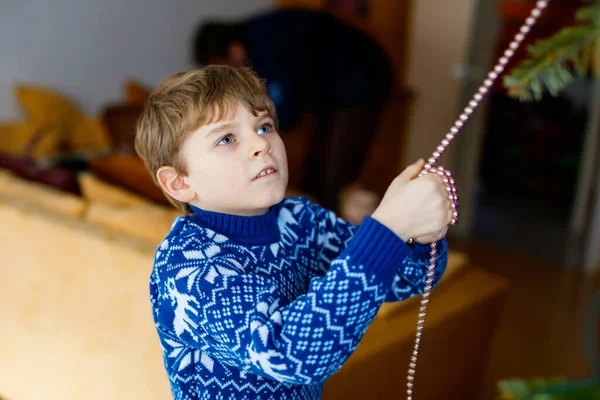 Liten pojke och hans pappa tar ner julpynt från julgranen. Far i bakgrunden. Familj efter firande ta bort och kassera träd. Pojkar i festliga kläder med ren — Stockfoto