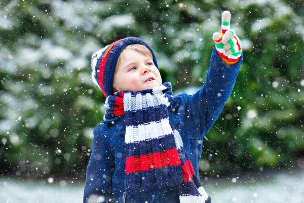 Cute little funny child in colorful winter fashion clothes having fun and playing with snow, outdoors during snowfall. Active outdoors leisure with children. Kid boy and toddler catching snowflakes. — Stock Photo, Image