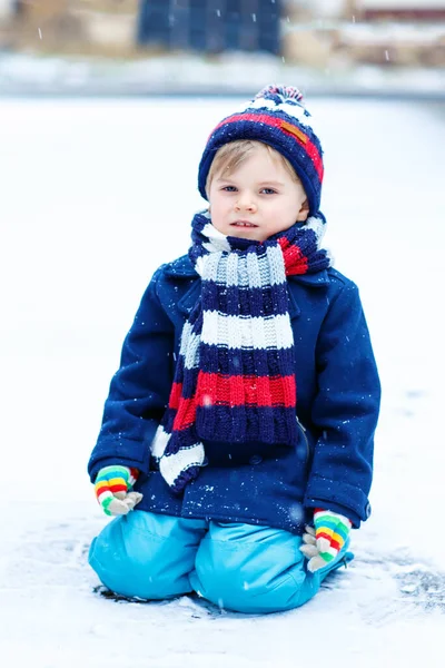 Cute little funny dziecko w kolorowe ubrania mody zimowej zabawy i zabawy ze śniegiem, na zewnątrz podczas opadów śniegu. Aktywny wypoczynek na świeżym powietrzu z dziećmi. Chłopiec i maluch łapie płatki śniegu. — Zdjęcie stockowe