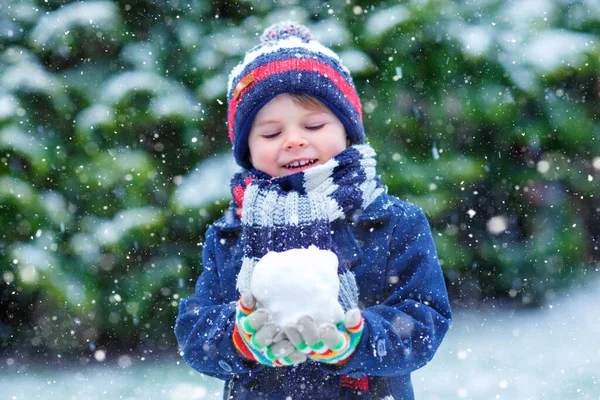 Söt liten rolig barn i färgglada vinter mode kläder har roligt och leka med snö, utomhus under snöfall. Aktiv friluftsliv med barn. Grabben och barnet fångar snöflingor. — Stockfoto