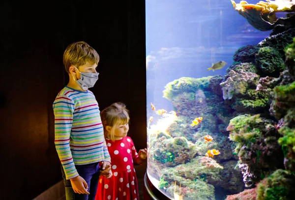Ragazzo e bambina che visitano insieme l'acquario dello zoo. Due bambini che guardano pesci, coralli e meduse. Bambino della scuola che indossa maschere mediche a causa del tempo pandemico del virus della corona. Famiglia in soggiorno — Foto Stock