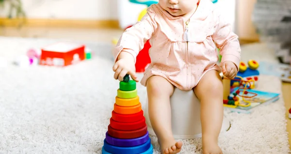 Closeup of cute little 12 months old toddler baby girl child sitting on potty. Kid playing with educational wooden toy. Toilet training concept. Baby learning, development steps