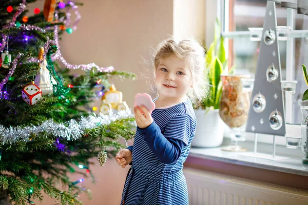 Adorabile bambina che tiene piccolo specchio e in piedi vicino all'albero di Natale d. Bambino in abiti festivi celebrazione di Natale — Foto Stock