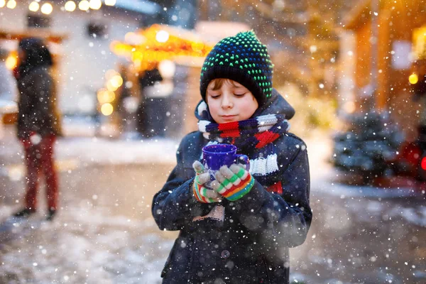 Little cute kid boy drinking hot children punch or chocolate on German Christmas market. Happy child on traditional family market in Germany, Laughing boy in colorful winter clothes — Stock Photo, Image