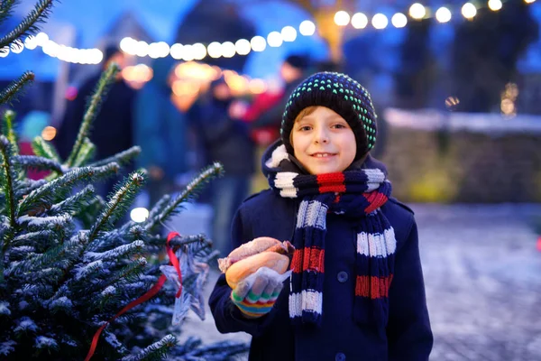 Kleiner süßer Junge isst deutsche Wurst und trinkt heißen Kinderpunsch auf dem Weihnachtsmarkt. Glückliches Kind auf dem traditionellen Familienmarkt in Deutschland. Lachender Junge in bunter Winterkleidung — Stockfoto