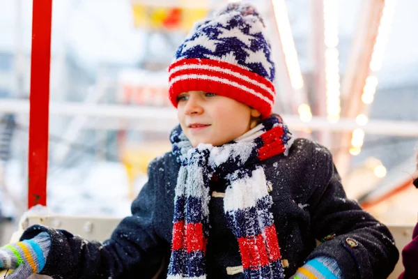 Little lovely kid boy having fun on ferris wheel on traditional German Christmas market during strong snowfall. Happy healthy child enjoying family market in Germany. Lovely schoolboy. — Stock Photo, Image