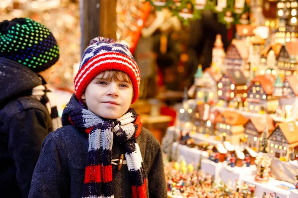 Zwei kleine Jungen suchen Dekoration auf dem Weihnachtsmarkt aus. Schöne Geschwister und beste Freunde kaufen Spielzeug und dekorative Häuser. Weihnachtsmarkt in Deutschland. — Stockfoto