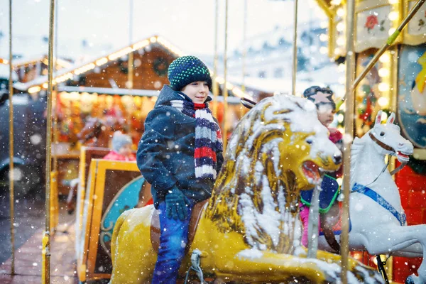 Adorable little kid boy riding on a merry go round carousel horse at Christmas funfair or market, outdoors. Happy child having fun on traditional family xmas market in Germany — Stock Photo, Image