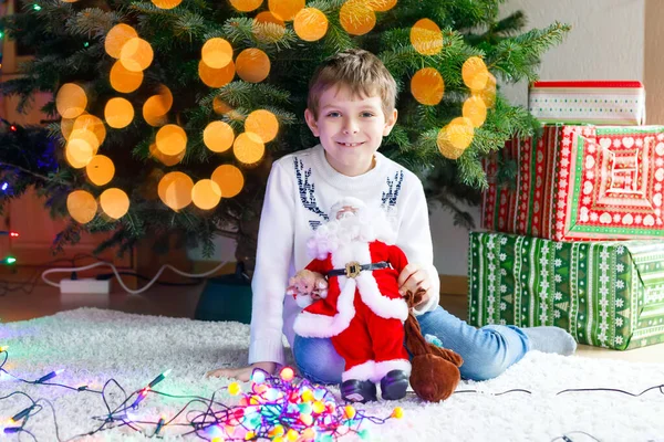 Entzückende kleine Mädchen und Bruder mit bunten Lichtergirlanden und Spielzeug-Weihnachtsmann in niedlichen Händen. — Stockfoto