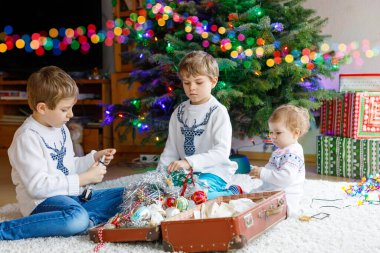 İki küçük oğlan ve sevimli kız bebek Noel ağacını eski model oyuncaklar ve toplarla süslüyorlar. Aile tatili için aile hazırlık kutlaması. Evde üç çocuk, erkek ve kız kardeş var..