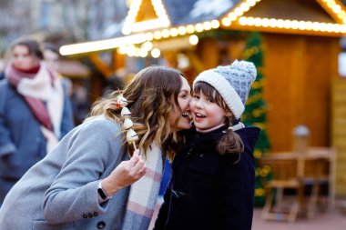 Anne ve kızı geleneksel Alman Noel pazarında beyaz çikolata kaplı meyve ve çilek yiyorlar. Karlı bir günde Almanya 'da geleneksel aile pazarında mutlu kız ve kadın