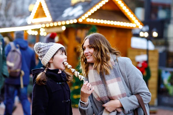 Matka a dcera, kteří jedli bílou čokoládu, pokrývali ovoce a jahody na špejli na tradičním německém vánočním trhu. Šťastná dívka a žena na tradičním rodinném trhu v Německu během zasněženého dne — Stock fotografie
