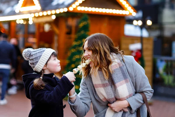 在传统的德国圣诞市场上，母亲和女儿吃着覆盖着水果和草莓的白色巧克力。德国传统家庭市场上下雪天快乐的女孩和女人 — 图库照片