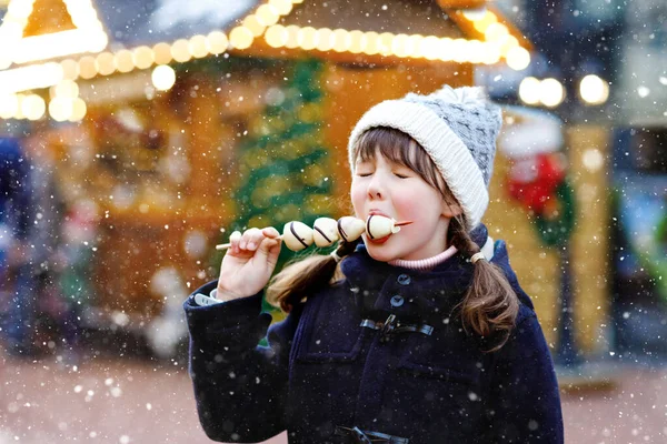 Petite fille mignonne mangeant des fraises couvertes de chocolat blanc sur brochette sur le marché de Noël allemand traditionnel. Enfant heureux sur le marché familial traditionnel en Allemagne pendant la journée enneigée. — Photo