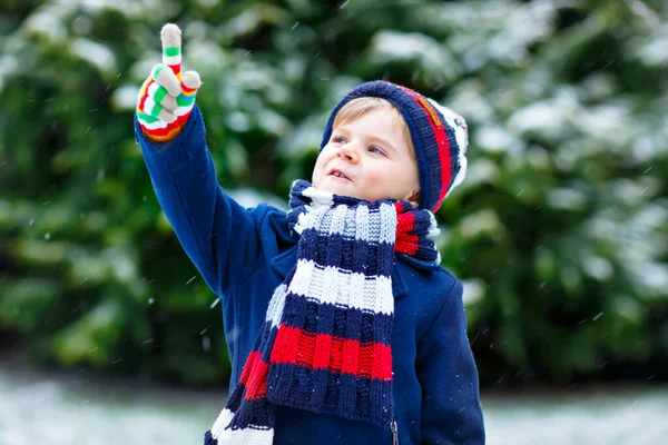 Aranyos kis vicces fiú színes téli divat ruhák szórakozás és játszik a hó, szabadban hóesés közben — Stock Fotó