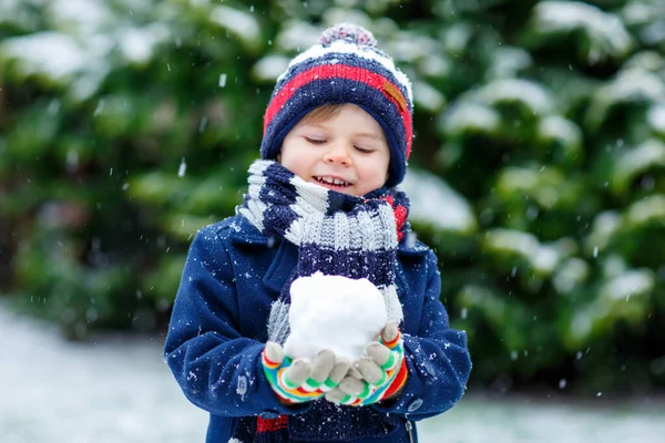 Söt liten rolig pojke i färgglada vinter mode kläder har roligt och leka med snö, utomhus under snöfall — Stockfoto