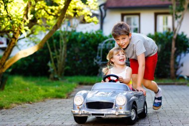 İki mutlu çocuk açık havada, yaz bahçesinde eski oyuncak arabalarıyla oynuyorlar. Çocuk itip kakıyor ve içinde küçük bir kız, içinde de tatlı bir kız kardeşi olan arabayı sürüyor. Gülen ve gülümseyen çocuklar. Güzel aile.