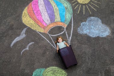 Küçük mutlu kız sıcak hava balonuyla uçuyor gökkuşağı renklerinde renkli tebeşirlerle boyanmış yerde veya yazın asfaltta. Sevimli çocuk eğleniyor. Çocuklar için yaratıcı eğlence.