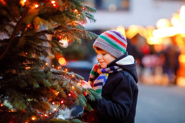 Küçük şirin çocuk şiddetli kar yağışında geleneksel Noel pazarında eğleniyor. Mutlu çocuk Almanya 'da geleneksel aile pazarının tadını çıkarıyor. Aydınlatılmış xmas ağacının yanında duran öğrenci.. — Stok fotoğraf
