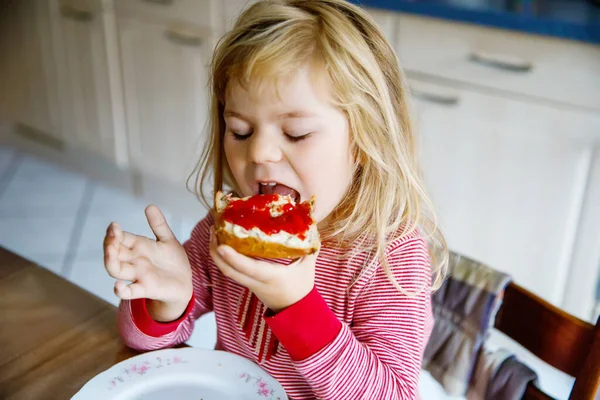 かわいい面白い幼児の女の子は朝食のために甘いパンを食べる。幸せな子供はイチゴジャムとパンロールを食べる。自家製ゼリーのある子供や子供のための健康食品 — ストック写真