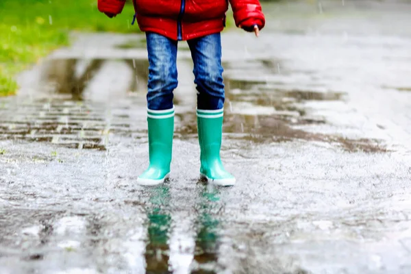 Detailní záběr dítěte ve žlutých holínkách do deště a chůzi během lijáku, deště a sněhu za chladného dne. Dítě v barevné módní ležérní oblečení skákání v louži. Bavíte se venku — Stock fotografie