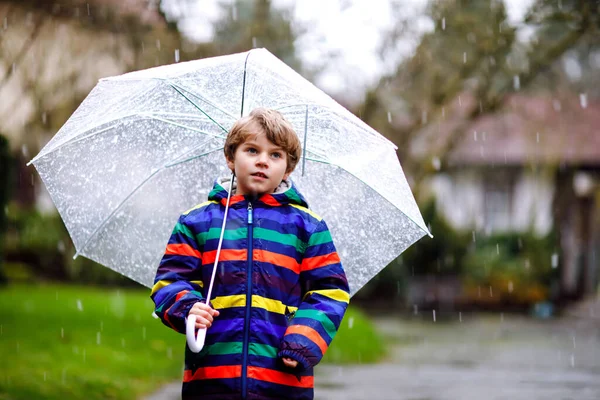 Hermoso niño en camino a la escuela caminando durante el aguanieve, la lluvia y la nieve con un paraguas en el día frío. Niño feliz y alegre en ropa casual de moda colorida. — Foto de Stock