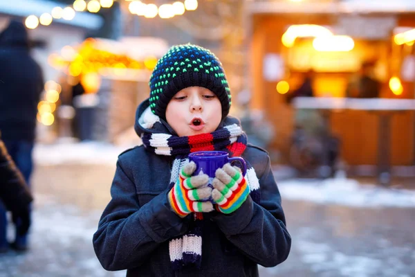 Niño lindo bebiendo ponche de niños calientes o chocolate en el mercado de Navidad alemán. Niño feliz en el mercado familiar tradicional en Alemania, niño risueño en ropa de invierno colorida — Foto de Stock