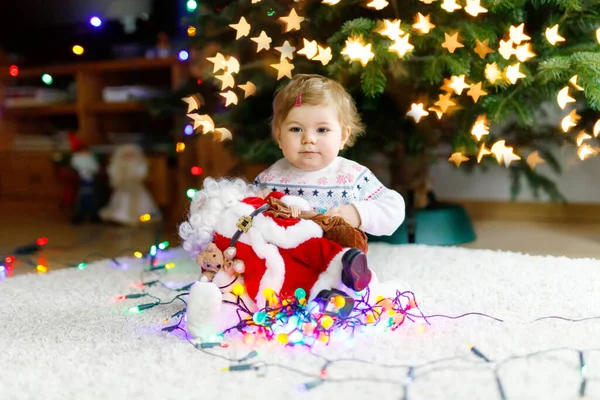 형형색색의 조명을 귀여운 손으로 들고 있는 사랑 스러운 어린 소녀. 크리스마스 트리를 가족들로 장식하는 축제 복을 입은 어린아이. 웨 덴 나크 텐이라고 불리는 전통 명절의 첫 번째 기념행사 — 스톡 사진