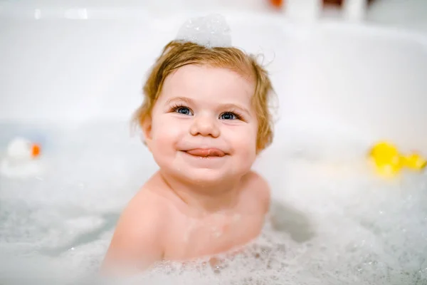 Schattig schattig baby meisje neemt schuimig bad in bad. Peuter spelen met bad rubber speelgoed. Mooi kind hebben plezier met kleurrijke kauwgom speelgoed en schuim bellen — Stockfoto